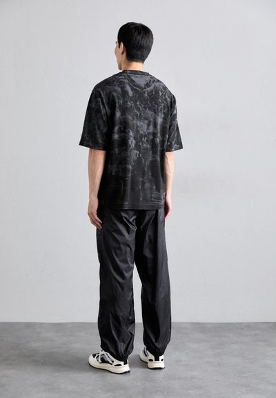 Zwarte shirt met korte mouwen en een textuurpatroon, gecombineerd met losse zwarte broek en witte sneakers. Eenvoudig, functioneel ontwerp zonder versieringen.
