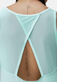 Mintgroene sporttop met een mesh achterkant, featuring een kruislings ontwerp en een gladde textuur. Laat de huid eronder zien met een afgeronde zoom.