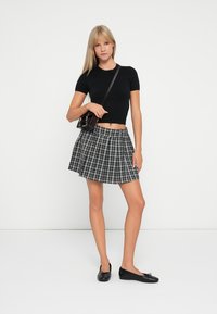 Top nero aderente a maniche corte abbinato a una gonna plissettata a righe bianche e nere, con lunghezza fino a metà coscia. Indossato con scarpe ballerine nere e una borsa piccola.