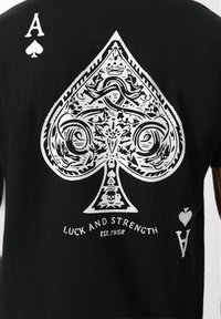 Črna majica s čudovitim belim motivom z velikim Asom pik in napisom "Sreča in moč UST. 1958" pod njim.