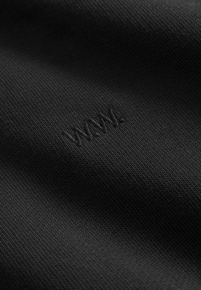 Mustrist kootud kangas, millel on peen tekstuur ja reljeefne "WMM." logo. Materjal näeb välja pehme ja vastupidav.
