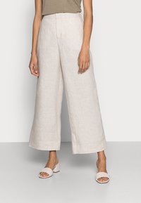 Jasne beżowe spodnie typu wide-leg z lnu z wysokim stanem. Zestawione z jasnobeżowymi plecionymi klapami. Gładka tekstura.