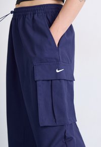 Tamno plave cargo hlače izrađene od lagane tkanine, s bočnom džepom, elastičnim pojasom i malim bijelim Nike logotipom na džepu.