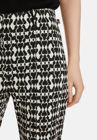 Schwarz-weiße gemusterte Hose mit geometrischem Design, mit einem Kordelzugbund, Seitennähten und glatter Stoffoberfläche.