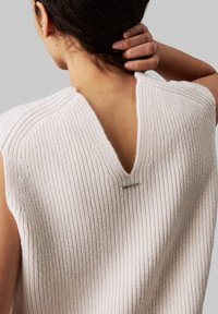 Haut sans manches en tricot rose clair avec un dos en V profond et un accent métallique. Le matériau à côtes texturé ajoute un intérêt visuel.