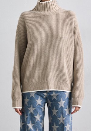 Maglione a collo alto beige a righe abbinato a jeans blu con grandi motivi a stella bianchi.