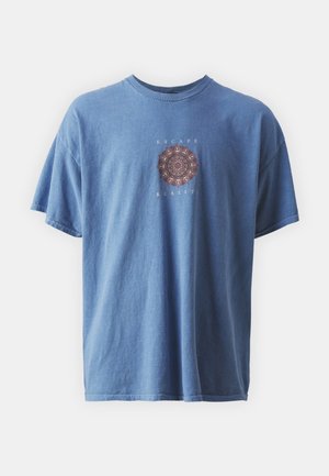 T-shirt en coton bleu à coupe décontractée, présentant un graphisme mandala et le texte « ESCAPE REALITY » en blanc, manches courtes, et col rond.