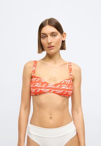 Pomarańczowy top bikini z białym, odręcznym napisem, szerokimi ramiączkami i zaokrąglonym dekoltem; połączony z białym, wysokim dołem bikini.