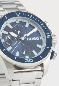 Stainless steel watch with a navy blue dial, silver subdials, date display, and luminous markers. Features a metallic bracelet and blue bezel.