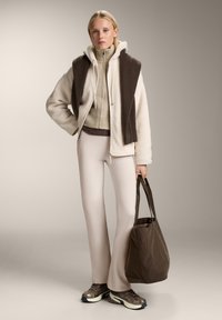 Giacca in finta pelliccia beige sopra un maglione marrone a costine, abbinata a pantaloni crema a vita alta, sneakers marroni e una borsa a tracolla marrone.