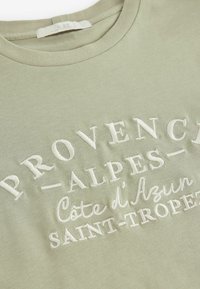 Svijetlozeleni pamučni majica s okruglim izrezom, s reljefnim bijelim tekstom: "PROVENCE-ALPES-Côte d'Azur SAINT-TROPEZ".