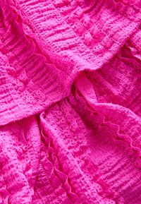 Tissu rose vif à surface texturée et froissée avec des volants en dentelle à œillets décoratifs disposés en plis doux.