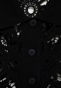 Black lace shirt with a textured design, featuring a floral pattern, a collared neckline, and five small black buttons down the front.