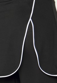 Svart atletisk kjol med en rundad fåll, prydd med vit piping längs kanterna. Tyget verkar slätt och elastiskt.