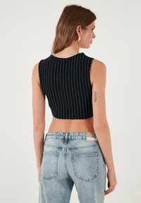 Jūras karafāna ir ar baltām vertikālām svītrām, augsta kakla un piedurknēm bez dizains, apvienota ar izbalējušiem zilajiem augsto jostasvietu džinsiem.