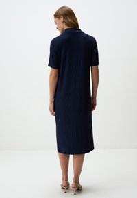 Abito corto blu navy con maniche corte realizzato in tessuto testurizzato, caratterizzato da un colletto e una lunghezza intermedia. Indossato con sandali con tacco beige.