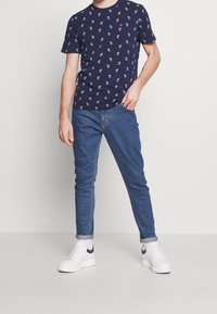 T-shirt a maniche corte blu navy con motivi bianchi, abbinato a jeans azzurri chiari e sneakers bianche con dettagli blu navy.
