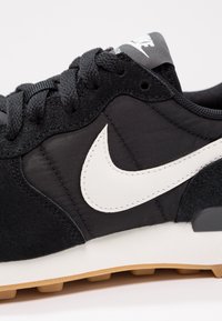 Gros plan d’une basket Nike noire avec logo Swoosh blanc, lacets noirs et semelle intermédiaire blanche avec semelle extérieure en caoutchouc couleur gomme.