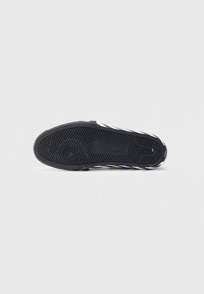 Suola di sneaker nera in gomma con un motivo a spina di pesce e accenti di strisce bianche, caratterizzata da una superficie testurizzata e un dettaglio con logo circolare.