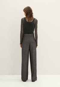 Un haut noir scintillant à manches longues associé à un pantalon gris taille haute et ample. Texture lisse, coupe détendue, avec des ourlets de manches légèrement effilochés.