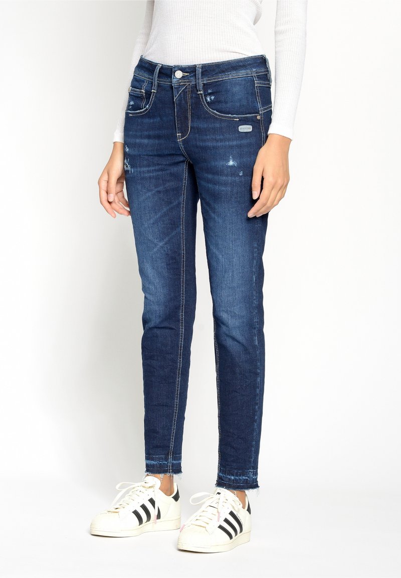 Tunna blå denimjeans med lätt slitage, fem fickor och kontrasterande sömmar. Matchas med vita sneakers med svarta ränder.