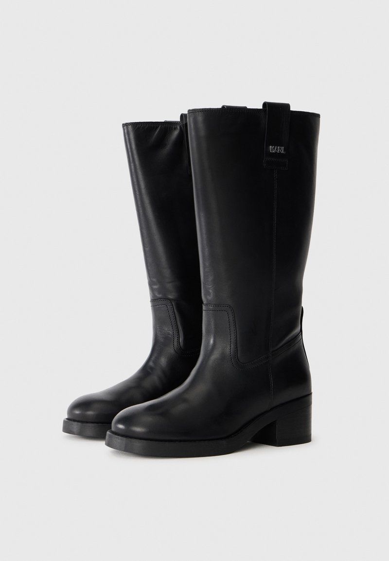 Bottes en cuir noir jusqu'au genou avec un léger talon, bout arrondi et texture lisse. Caractérisées par une languette sur le côté pour un enfilage facile.