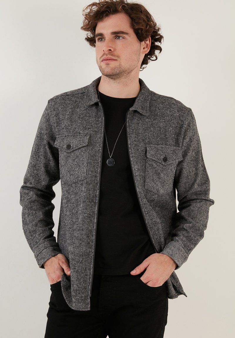 Grijze flanellen shirt met een knoopsluiting aan de voorkant, twee borstzakken en een kraag; heeft een gestructureerd patroon en lange mouwen.