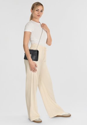 Pantaloni beige leggeri a gamba larga con un elastico in vita, abbinati a una t-shirt bianca aderente e a una piccola borsa a tracolla nera.