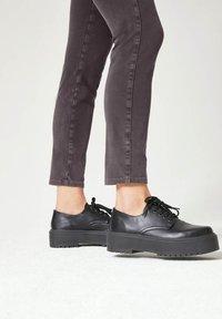 Zwarte leren platform schoenen met een ronde neus, vetersluiting en een dikke rubberen zool; gedragen met grijze fitted broek.