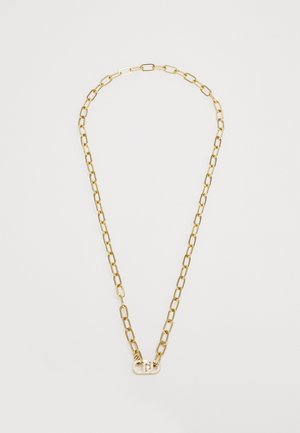 Zlatna metalna lančić ogrlica s produženim zrncima, koja ima dekorativnu kopču s prozirnim dragim kamenom akcentom u središtu.