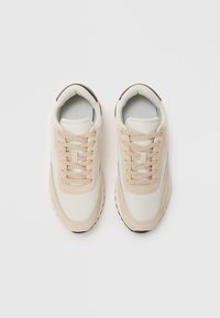 Bež tenisice s teksturiranim nubukom i glatkim platnom, okruglim vrhom i ravnim vezicama, s kontrastnim tamnim potplatima.