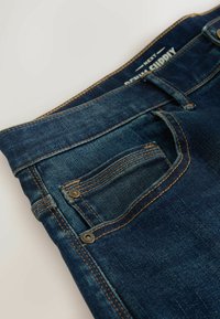 Tumedat sinised teksad kontrastsete oranžide õmbluste, väikese esikoti ja tavaliste vöökohaga, kergelt pleekinud lõpetusega.