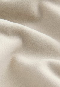 Heled pruun fleece kangas pehme ja tekstureeritud pinnaga, millel on õrnad lained ja kortsud, illustreerides selle kerget ja sooja iseloomu.