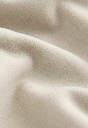 Hellbeige Fleece-Stoff mit einer weichen, strukturierten Oberfläche, die sanfte Wellen und Falten zeigt und seine leichten sowie warmen Eigenschaften veranschaulicht.