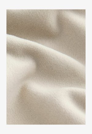 Hellbeige Fleece-Stoff mit einer weichen, strukturierten Oberfläche, die sanfte Wellen und Falten zeigt und seine leichten sowie warmen Eigenschaften veranschaulicht.