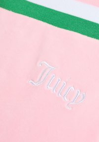 Roze velours stof heeft een groene en witte gestreepte ribboord. "Juicy" is in het wit geborduurd, wat een zachte textuur toont.