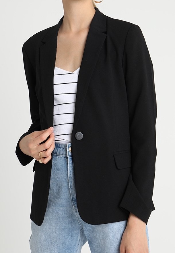 Blazer noir avec revers crantés, fermeture à un bouton et deux poches avant, porté sur un haut rayé blanc et noir.