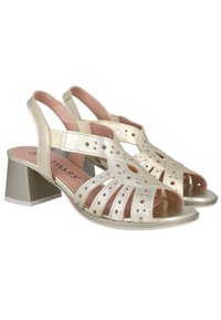 Sandalias abiertas de dedos en metal dorado con un tacón grueso, que cuentan con patrones recortados y una plantilla acolchada. Diseño tipo slingback con correas elásticas.