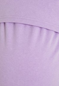 Ljust lila tyg med en mjuk textur och en samlad detalj. Sömmarna är synliga längs den övre kanten.