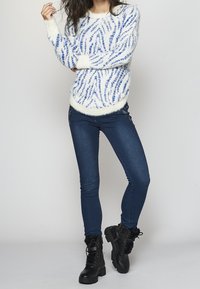White fuzzy sweater with blue zigzag pattern, paired with dark blue skinny jeans and black lace-up boots with faux fur accents.