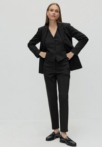 Svart randig kostym med en figursydd väst och skräddarsydda byxor, parat med blanka svarta loafers. Slät tyg med en strukturerad design.