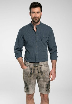 Gestreiftes navy-blaues Hemd mit langen Ärmeln, kombiniert mit grauen Lederhosen mit floralen Stickereien und einem dekorativen Gürtel.