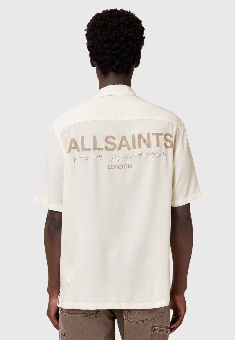 Rövid ujjú krémszínű ing, hátoldalán "ALLSAINTS" és "LONDON" feliratok barna betűkkel, valamint japán szöveggel. Sima tapintású.