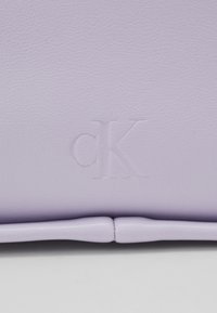 Fialová kožená taška s reliéfním logem "cK", hladkým povrchem a strukturovaným tvarem s bezpečným zapínáním.