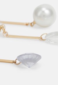 Orecchini in tono oro con una perla rotonda, una goccia trasparente e un gemma lavanda sfaccettata a forma di diamante. Superfici lisce e lucide.