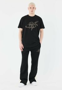Sæt bestående af en sort bomulds T-shirt og bukser med et gråt grafikdesign. Ensemblet har en afslappet pasform og er parret med hvide sneakers.