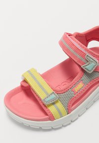 Rosa sandaler med mesh-overdel, grå og gule stropper, justerbare Velcro-lukkinger og en strukturert gummisåle med en fremtredende logo.