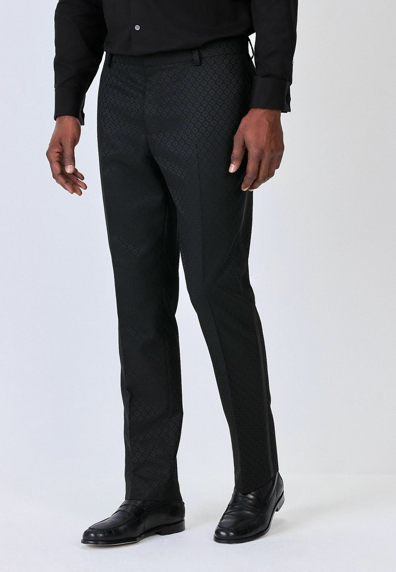 Pantaloni neri eleganti con un motivo a diamante testurizzato, design slim fit, chiusura con bottone e cerniera, abbinati a scarpe eleganti nere.