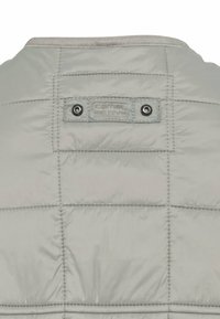 Helle graue Steppjacke mit gequilteter Textur, ausgestattet mit einem Camel Active-Logoetikett und zwei metallischen Druckknöpfen auf der Rückseite.