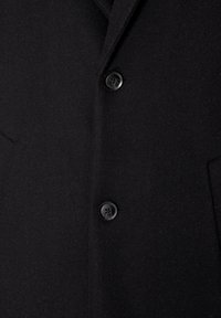 Manteau en laine noire avec deux boutons ronds noirs visibles et poches latérales, montrant la zone de fermeture avant.